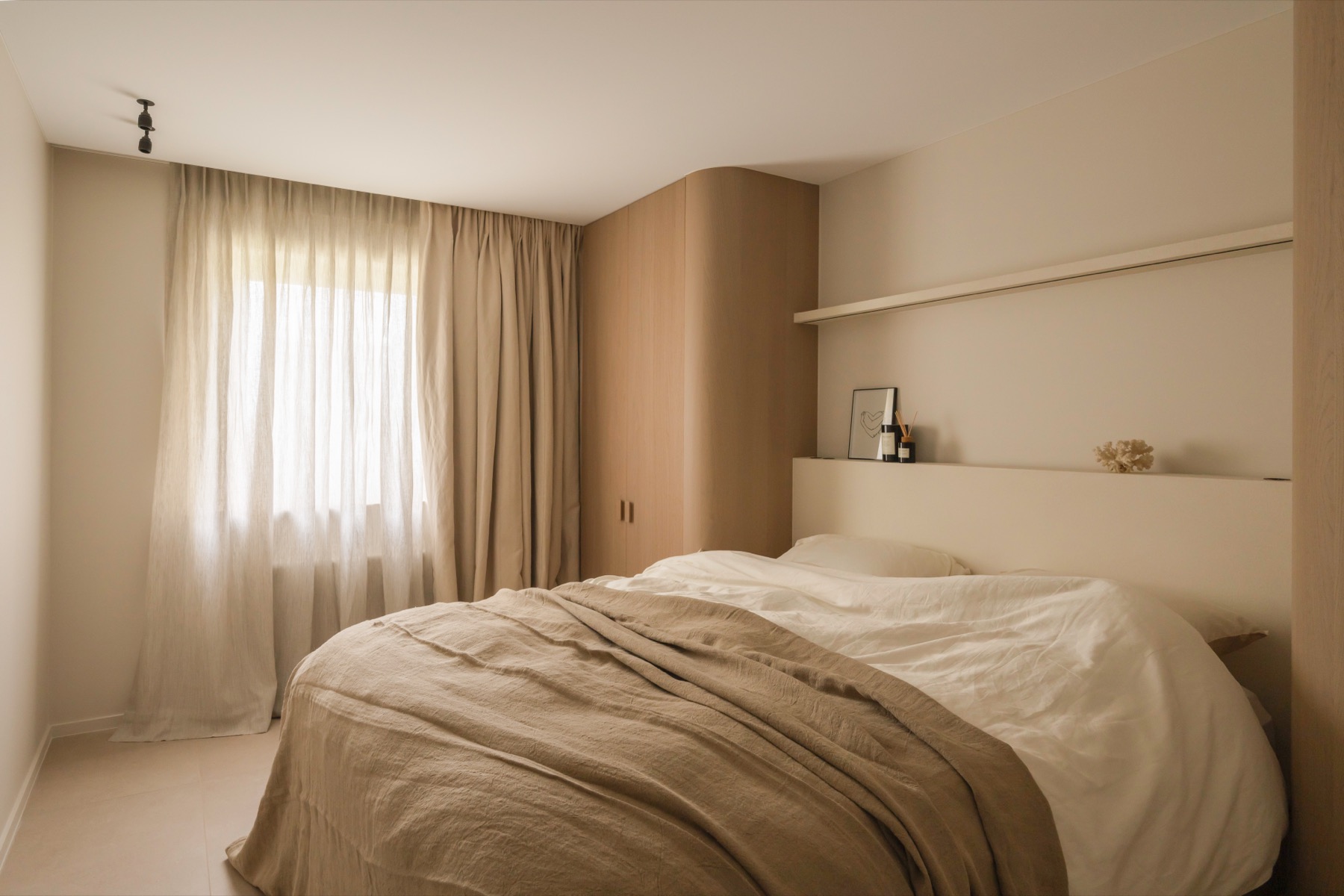 Slaapkamer met linnen beddengoed, zachte gordijnen en een afgeronde kastenwand